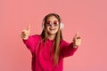 Enjoy favorite music. Girl in round glasses and wireless headphone point fingers at camera