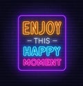 Enjoy This Happy Moment neon quote on a brick wall.