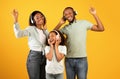 Enjoy music together. Happy african american family of three dancing in headphones, isolated on yellow background