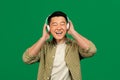 Enjoy the sound. Happy asian mature man wearing and touching wireless headset, enjoying song with closed eyes Royalty Free Stock Photo