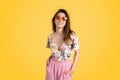 Enjoy summertime. Beautiful young lady in summer outfit and colorful sunglasses, smiling at camera, yellow background Royalty Free Stock Photo