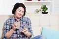 Enjoying coffee at home. Attractive young smiling woman sitting on sofa at home and holding coffee cup and phone, after hard week