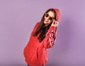 Enjoying excited smiling sporty woman lookig happy in fashion red hoodie and sunglasses on purple bright background with empty Royalty Free Stock Photo