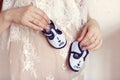 Enjoying future life. Pregnant woman holding small baby booties at her belly, closeup Royalty Free Stock Photo