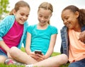 Enjoying her new phones functions. Three little girls spending time together and sharing a smartphone while outdoors. Royalty Free Stock Photo