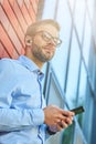 Enjoying music. Young handsome businessman wearing wireless earphones holding smartphone and looking away while leaning Royalty Free Stock Photo