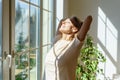 Happy senior woman enjoying life, standing in front of window with closed eyes and smiling Royalty Free Stock Photo