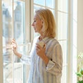 Beautiful senior woman with cup of coffee looking in window while enjoying new day at home Royalty Free Stock Photo