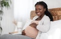 Enjoying Pregnancy. Cheerful Black Pregnant Woman Resting In Bed, Touching Her Belly Royalty Free Stock Photo
