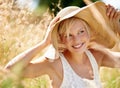 Enjoying the summer sunshine. Beautiful young woman wearing a straw hat and standing in a field. Royalty Free Stock Photo