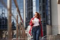 Enjoying sunlight at cloudy day. Adult pretty woman in warm red coat have walk in the city at her weekends time