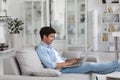 Enjoying time at home. Handsome young man sitting on the couch In a living room with laptop, freelancer Royalty Free Stock Photo