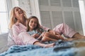 Enjoying time together. Beautiful young mother embracing her daughter and smiling while sitting on the bed at home Royalty Free Stock Photo