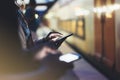 Enjoying travel. Young woman waiting on station platform on background light electric moving train using smart phone in night Royalty Free Stock Photo