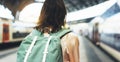 Enjoying travel. Young woman waiting on the station platform with backpack on background electric train. Tourist plan route