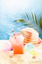 Enjoyment summertime beach vacation - picnic on tropical beach with cold fruit cocktail, sun hat, beach plays under palm leaves. Royalty Free Stock Photo