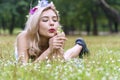 Enjoyment woman with flower on her hair blowing on dandelion flowers while lying on green grass in the park. Lovely girl Royalty Free Stock Photo