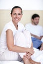 She enjoys the lazy mornings with her husband. A young woman sitting on a bed with her husband in the background.