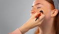 Enlarged photo. Girl with closed eyes, cosmetic powder is applied to her face with makeup brush. Grey background