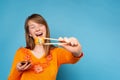 Enlarged photo of a happy blonde girl who with a smile holds sushi with wooden chopsticks and a bowl with sauce. Blue