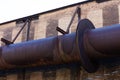 Enormous industrial pipe running along the exterior of a brick manufacturing warehouse, rusted metal and huge flanges riveted toge