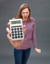 Enraged young woman screaming against financial economy on oversized calculator