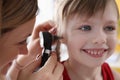 Ent doctor examining sore ear of small child using otoscope