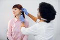 ENT doctor and patient in modern hospital. Female confident African American doctor doing ear examination with otoscope