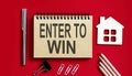 ENTER TO WIN text written on a notebook with pencils and office tools and model wooden house