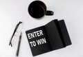 ENTER TO WIN written text in small black notebook with coffee , pen and glasess on white background. Black-white style