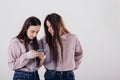 Enters something in the smartphone. Two sisters twins standing and posing in the studio with white background Royalty Free Stock Photo