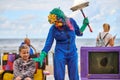 Entertainer in blue overalls and beast mask scaring little girl, outdoor costume festival at beach