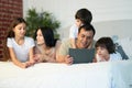 Entertainment. Happy latin family with cute little kids using digital tablet, lying on the bed together. Father looking Royalty Free Stock Photo