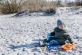 Enthusiast kid sits on a beach playing with sand. Fervid or fervent child dressed against the cold is sitting on a strand