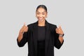 Enthusiastic African American woman in formal attire giving two thumbs up with a radiant smile