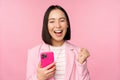 Enthusiastic asian businesswoman saying yes, winning on mobile phone, using smartphone and triumphing, celebrating Royalty Free Stock Photo