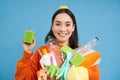 Enthusiastic asian girl showing cleaning sponge, holding empty plastic bottles, trash for recycling, sorting her
