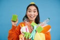 Enthusiastic asian girl showing cleaning sponge, holding empty plastic bottles, trash for recycling, sorting her