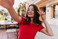 Enthusiastic caucasian lady making selfie in outdoor cafe. Laughing debonair woman taking picture of