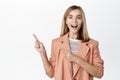 Enthusiastic little blond cute girl, small child in business blazer, pointing fingers left and smiling, showing banner Royalty Free Stock Photo