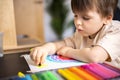 Enthusiastic male kid drawing multicolor rainbow paper sheet closeup early development art activity