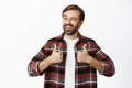 Enthusiastic male model winks and smiles, shows thumbs up, stands in checked shirt over white background