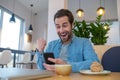 Enthusiastic man looking at smartphone sitting at table Royalty Free Stock Photo