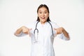 Enthusiastic medical staff, asian female healthcare worker, pointing fingers down and smiling amazed, showing discounts