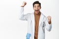 Enthusiastic medical worker, doctor in robe cheering, shouting from joy, winning, standing over white background