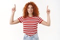Enthusiastic motivated good-looking redhead female curly hair smiling white teeth wear striped t-shirt pointing up Royalty Free Stock Photo