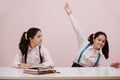 Enthusiastic perky schoolgirl raising a hand, her twin eyeing her with suspition Royalty Free Stock Photo