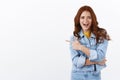 Enthusiastic sassy good-looking ginger girl with freckles in denim jacket pointing finger left, smiling amused and Royalty Free Stock Photo