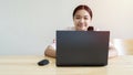 Enthusiastic schoolgirl engages in online studies using laptop sitting at table at home and smiling to camera Royalty Free Stock Photo