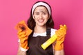 Enthusiastic smiling housewife holds dirty sponge and cleaning detergent, satisfied with result of cleaning, being dirty.